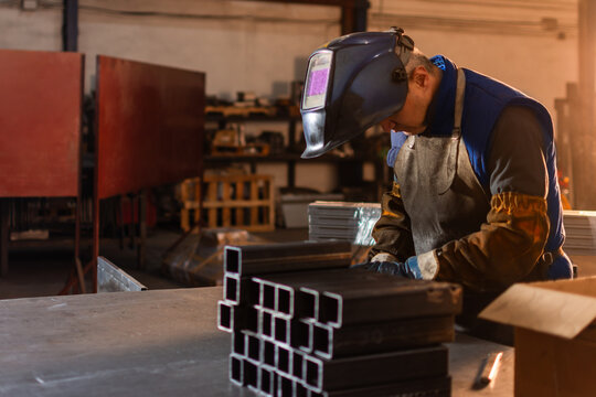 Metal pieces in foreground with welder preparing to weld