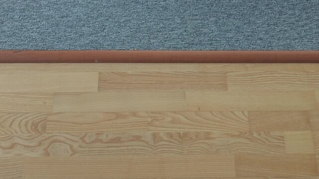 Steady camera movement backward, revealing the transition between a light wooden parquet floor and a gray textured carpet in an empty room