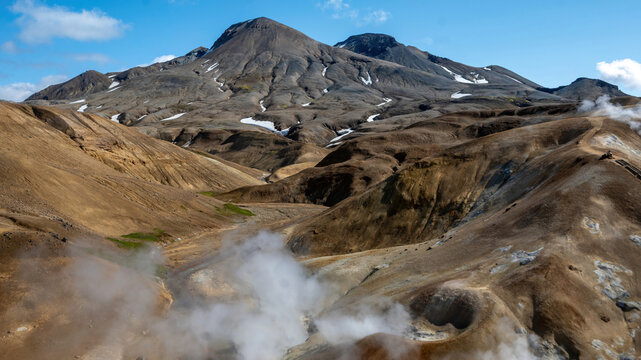 Steam rises from a geothermal vent beneath snow-streaked peaks at Kerlingarfjoll in the Icelandic Highlands, surrounded by rugged rhyolite mountains and valleys.