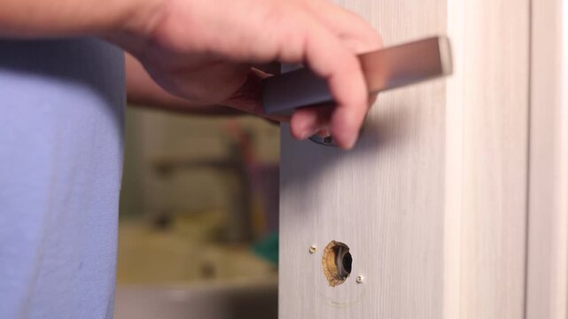 Horizontal 4K video. Male hand close up. Person installing or replacing metal handle on interior wooden door, fixing hardware mechanism during home renovation, DIY room upgrade project maintenance