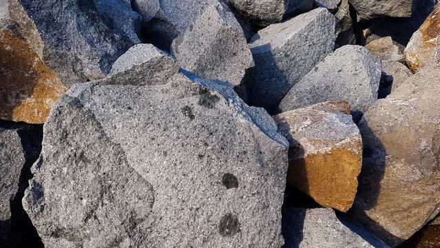 Texture of large gray granite boulders and rough stones piled together in bright daylight.