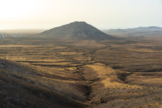 A sweeping aerial-like view from Mirador de Vallebron reveals eroded ravines and dirt tracks stretching toward the volcanic peak of Montana Tindaya, Fuerteventura, Canary Islands, Spain.