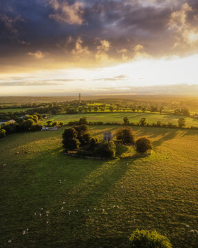 Aerial view of Caddell's Folly surrounded by lush green fields and trees under a dramatic sunset sky in County Meath, Ireland.