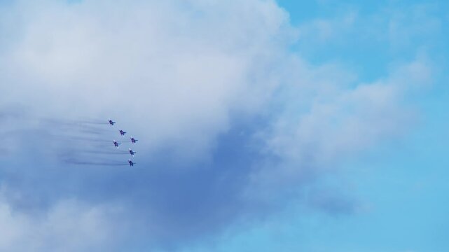 Colorful aircraft painted in USA flag colors leave thin exhaust trails while maintaining precise geometric pattern. Fighter jets fly in wedge. Aircraft feature USA flag colors.