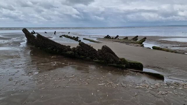 Wooden skeleton of an ancient shipwreck exposed at low tide on Cefn Sidan Beach in Pembrey Country Park, Carmarthenshire, South Wales, UK, maritime wreck stock video footage clip