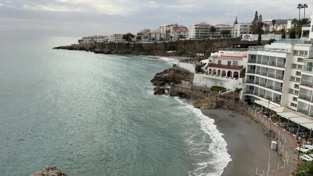 High angle drone shot capturing the Mediterranean architecture and rocky coastline of the historic seaside resort town of Nerja in Malaga, Spain.