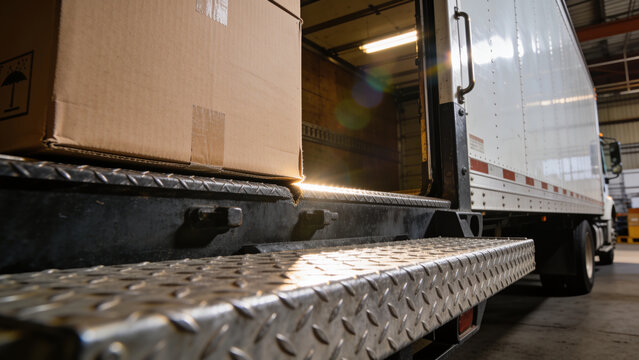 Truck tail lift being loaded with cardboard boxes at a warehouse loading dock, logistics and freight transport concept for shipping, delivery and supply chain operations.