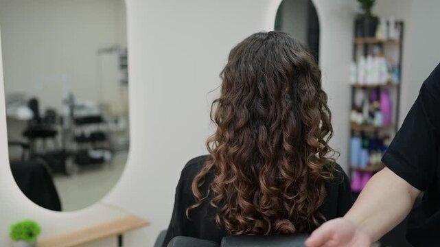 Hairdresser displays a client&rsquo;s finished curly hairstyle after professional styling, showing defined curls, volume and texture in a specialized curl salon.