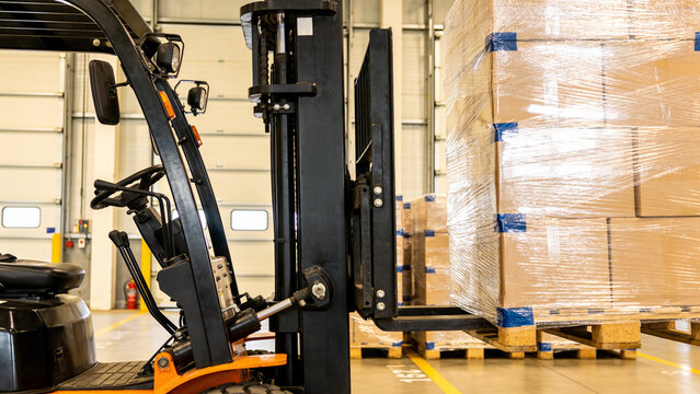 Forklift truck lifting a pallet stacked with shrink wrapped cardboard boxes in a bright warehouse loading bay, logistics and material handling concept