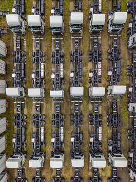 Aerial view of rows of new white truck chassis parked in an organized storage lot on muddy ground in Atsugi, Kanagawa, Japan.
