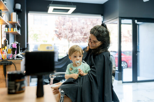 Mother holding toddler during haircut at barbershop