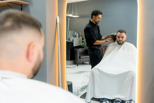 Barber trim client hair in modern barbershop mirror