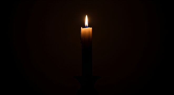 A single burning wax light glows gently in total darkness casting a warm yellow beam across the peaceful room while creating a serene atmosphere for quiet meditation and spiritual reflection