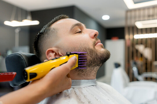 Barber trim beard with electric clipper in barbershop
