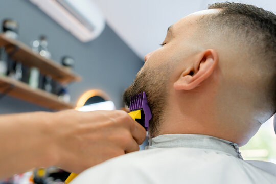 Barber trim beard of male client in modern barbershop