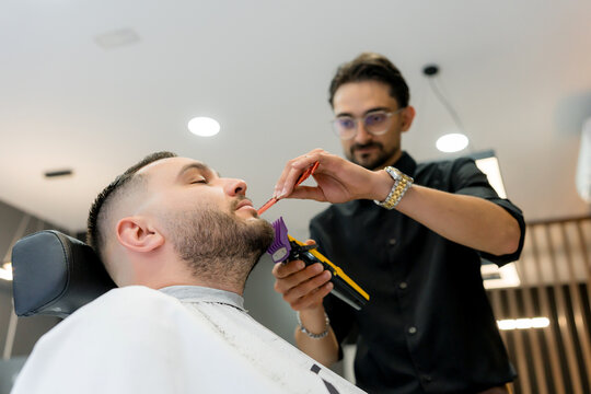 Barber trims client's beard with comb and clipper