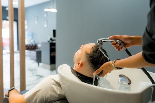 Barber rinse male client&rsquo;s hair at salon washbasin