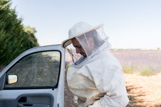 Beekeeper in protective suit beside vehicle at apiary