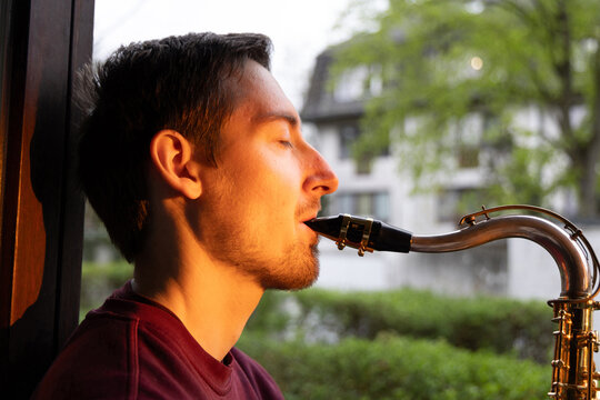 Man play saxophone by window in warm evening light