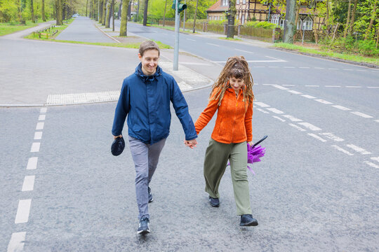 Couple cross street together in leafy residential neighborhood
