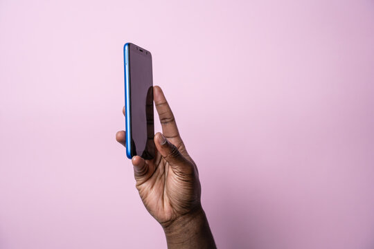 Black man hand hold smartphone against pink background