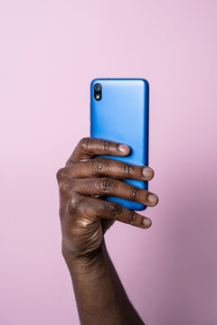 Black man hand hold blue smartphone against pink background