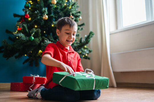 Boy open Christmas gift beside decorated tree at home