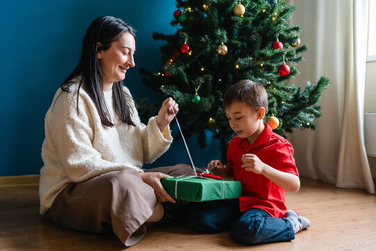 Mother and son unwrap Christmas gift by decorated tree