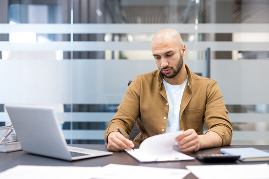 Productivity and business planning, focused man working on documents and laptop in modern office, Professional employee reviewing financial reports and analyzing data for corporate strategy