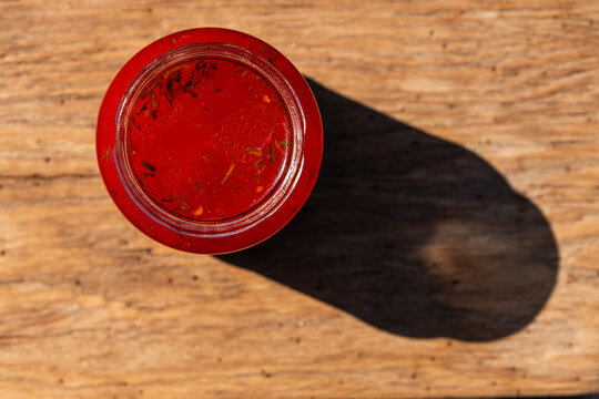 Top view of open glass jar with homemade red beetroot bouillon, closeup. Flat lay of round glass jar filled with fresh beetroot soup on rustic wooden surface under bright sunlight with long shadow