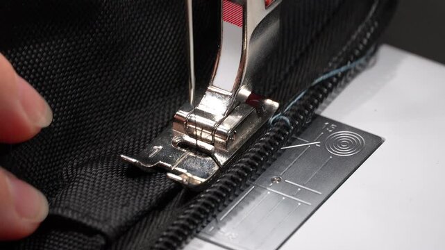 Slow motion close-up of a sewing machine stitching a zipper onto black fabric. Detailed view of the needle, zipper and fabric during the sewing process, suitable for tailoring, garment production, fas