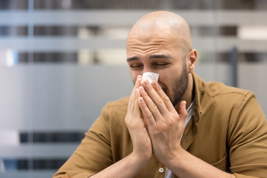 Cold and flu symptoms, man blowing nose into tissue with seasonal allergy or viral infection in office, Health issue and respiratory illness, employee suffering from sickness and discomfort