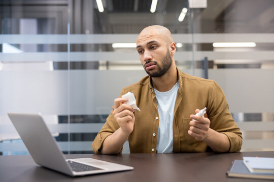 Workplace health and burnout, man using eye drops while working on laptop in office, Employee experiencing eye strain and dryness from prolonged screen time