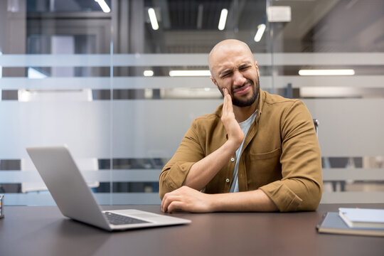 Toothache and dental pain at work, man suffering from oral health problem while sitting at office desk with laptop, Professional male experiencing severe jaw discomfort and facial pain