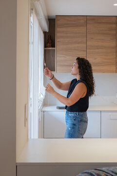 Woman adjust window blind in modern apartment kitchen