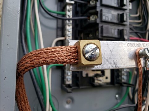 Close-up of a heavy braided copper grounding wire attached to a ground bus bar inside an electrical service panel for earth safety connection.
