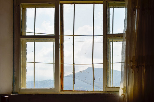 Old window overlooking mountain landscape through sheer curtain