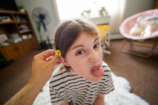 Child make funny face with flower behind ear at home