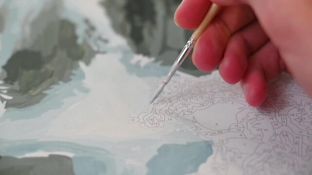 A hand uses a brush to paint with colorful watercolors