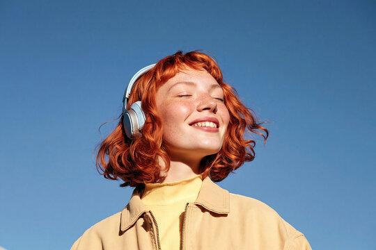 Cheerful Gen Z woman enjoy music with headphones outdoors