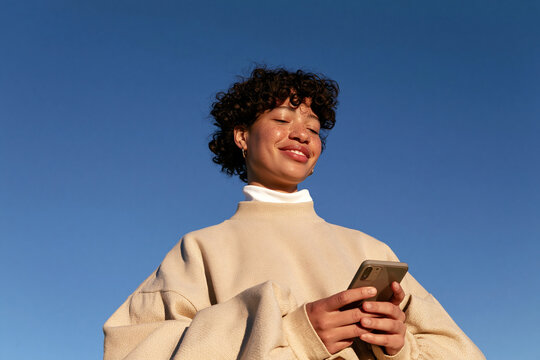 Cheerful Gen Z woman using smartphone in outdoor portrait