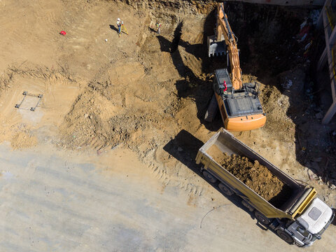 Aerial view of a construction site with an excavator digging into earth and a dump truck waiting to be loaded, with workers using surveying equipment in Istanbul, Istanbul, Turkiye.