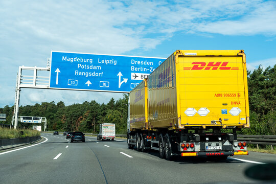 Germany - Aug 22, 2026: Yellow DHL road train in the right lane beneath blue direction boards naming Magdeburg, Leipzig, Potsdam, Rangsdorf, Dresden and Cottbus with a white van ahead
