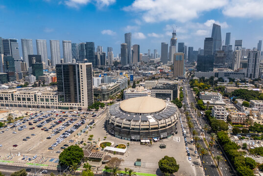 Aerial view of Menora Mivtachim Arena surrounded by urban infrastructure, parking lots, and the modern skyline of Tel Aviv-Yafo, Tel Aviv District, Israel.