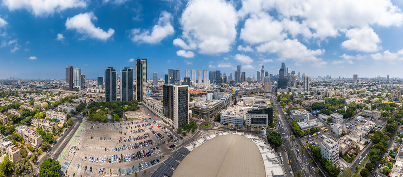 Aerial view of Menora Mivtachim Arena surrounded by modern skyscrapers, urban streets, and parking lots under a bright blue sky in Tel Aviv-Yafo, Tel Aviv District, Israel.