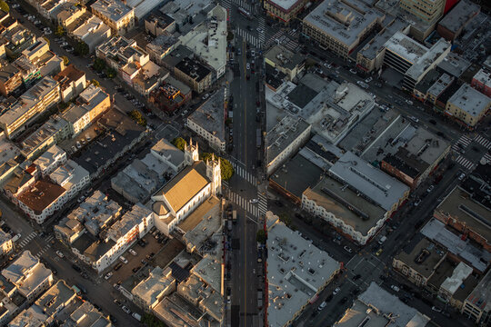 Aerial view of Saints Peter and Paul Church surrounded by historic urban buildings and streets during golden hour in San Francisco, California, United States.