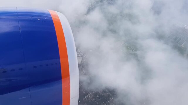 Airplane engine view through window during descent. Jet turbine over city and green landscape covered with clouds. Air travel and flight approach concept.
