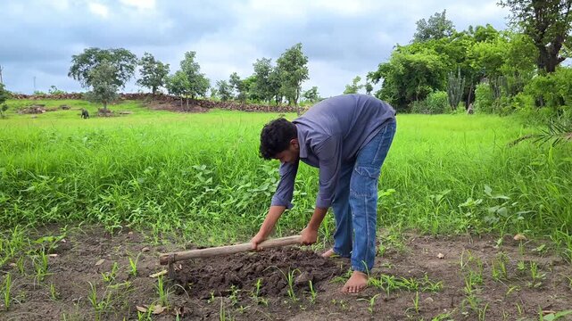 Young indian farmer digging soil with hoe tool for gardening pot