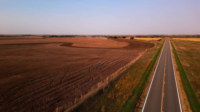 Golden hour aerial over a harvested field beside a country highway