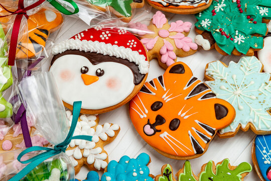 Colorful decorated holiday gingerbread cookies wrapped in clear plastic bags. Assorted frosted biscuits featuring festive figures lie on a white wooden surface.